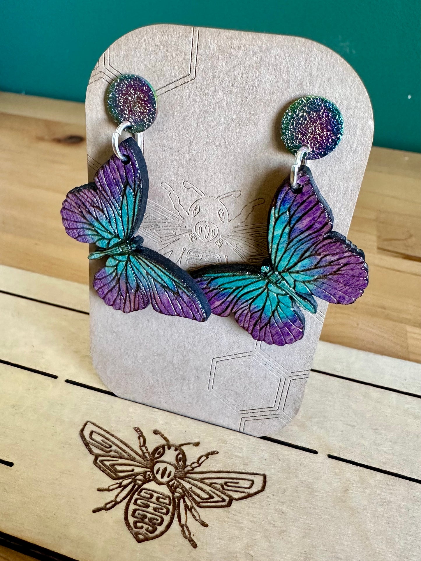 Dark to light shades of Blue and purple Wood Butterfly Earrings on silver colored hoops and purple and blue glittery stud earrings.