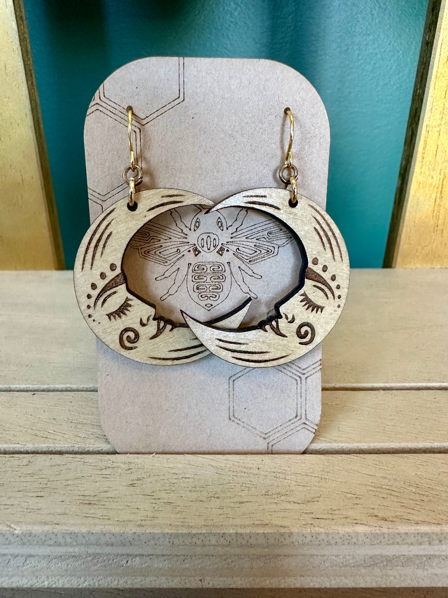 crescent moon natural wood earrings on gold colored hypoallergenic earring hook. Earrings on a brown card stock earring holder.