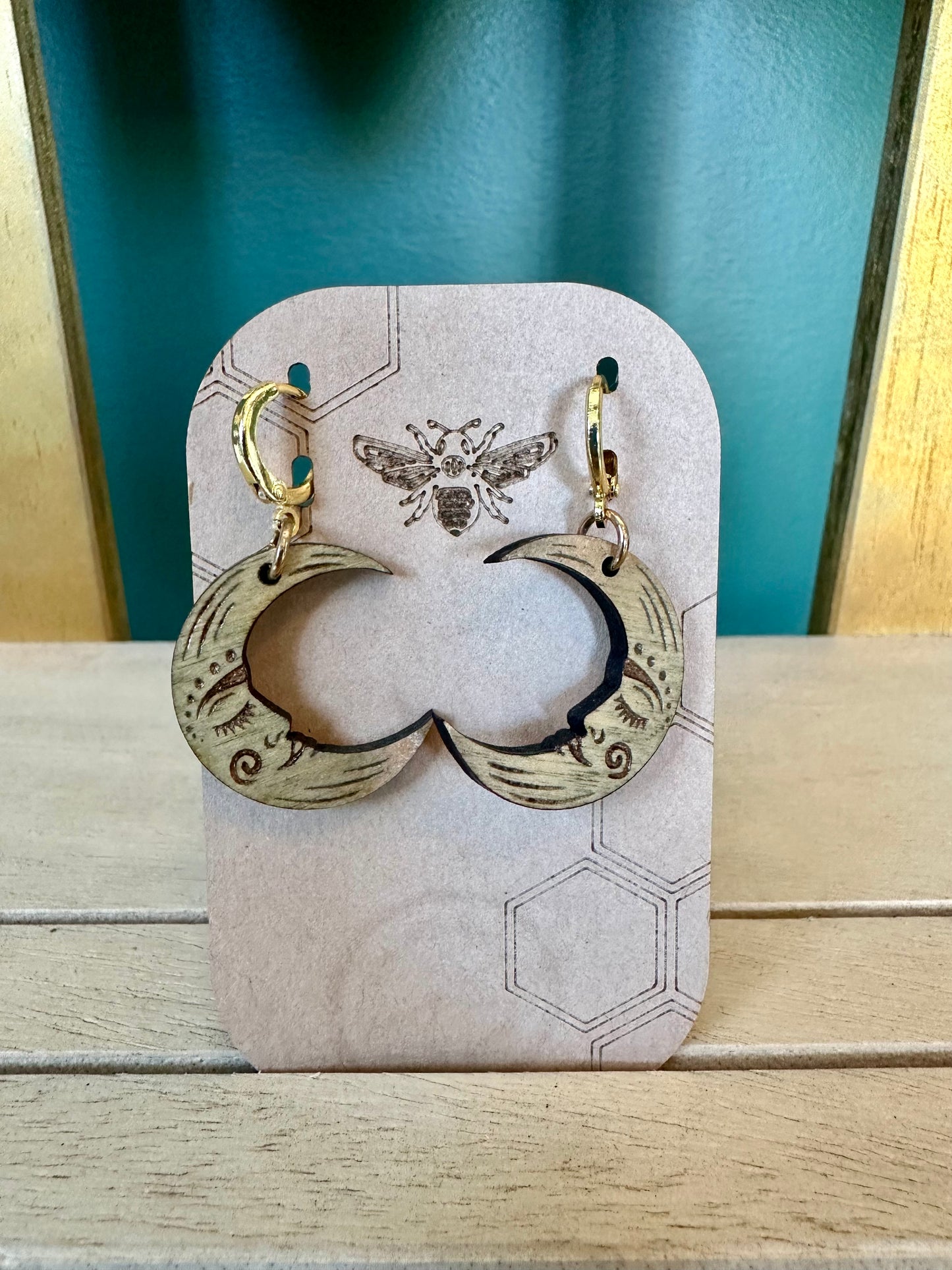 grey crescent moon with face wood earrings on gold colored hypoallergenic earring hoop. Earrings on a brown card stock earring holder.