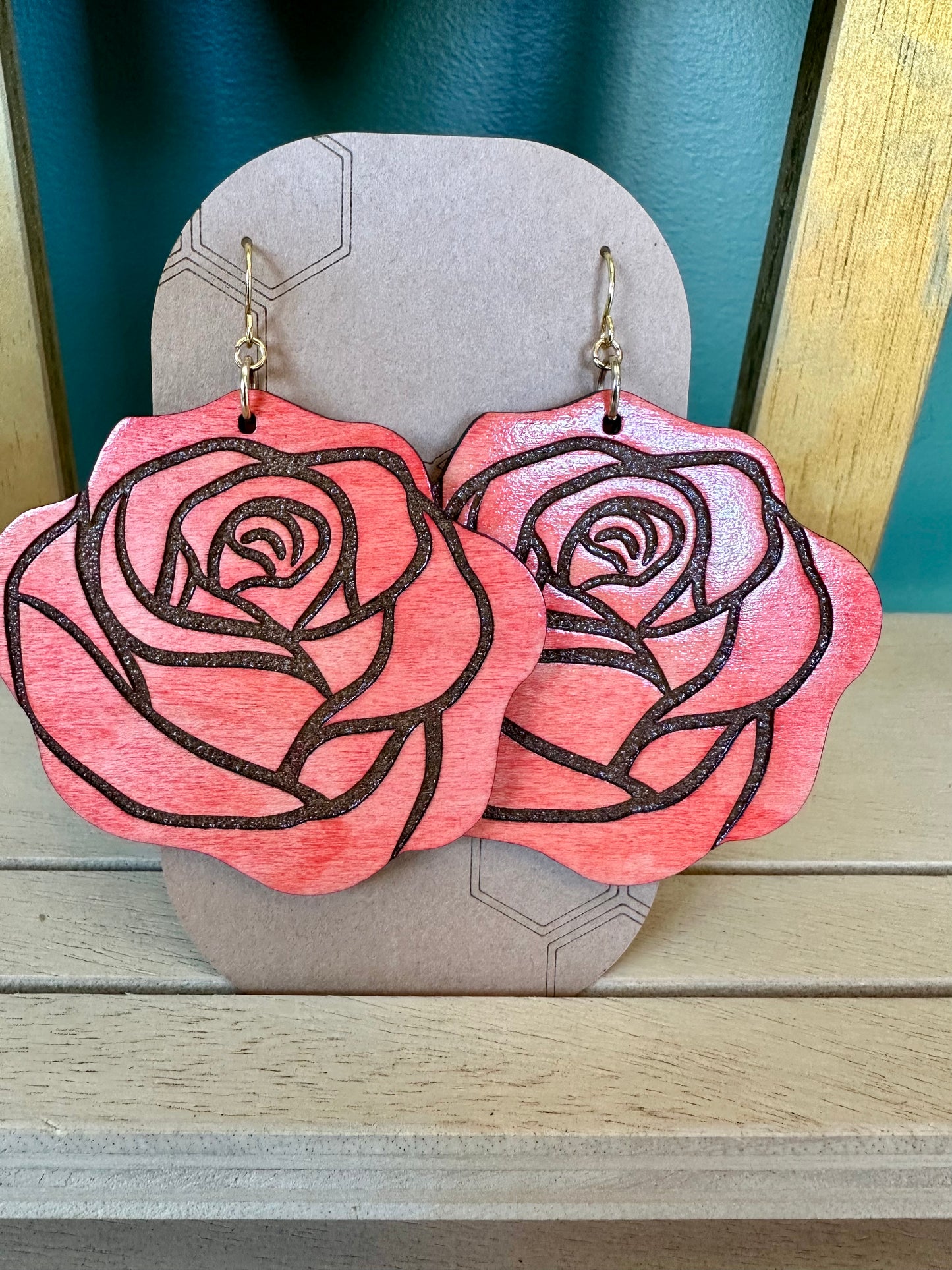 wood engraved light pink colored rose earrings on gold colored hypoallergenic earring hook. Earrings on a brown card stock earring holder.