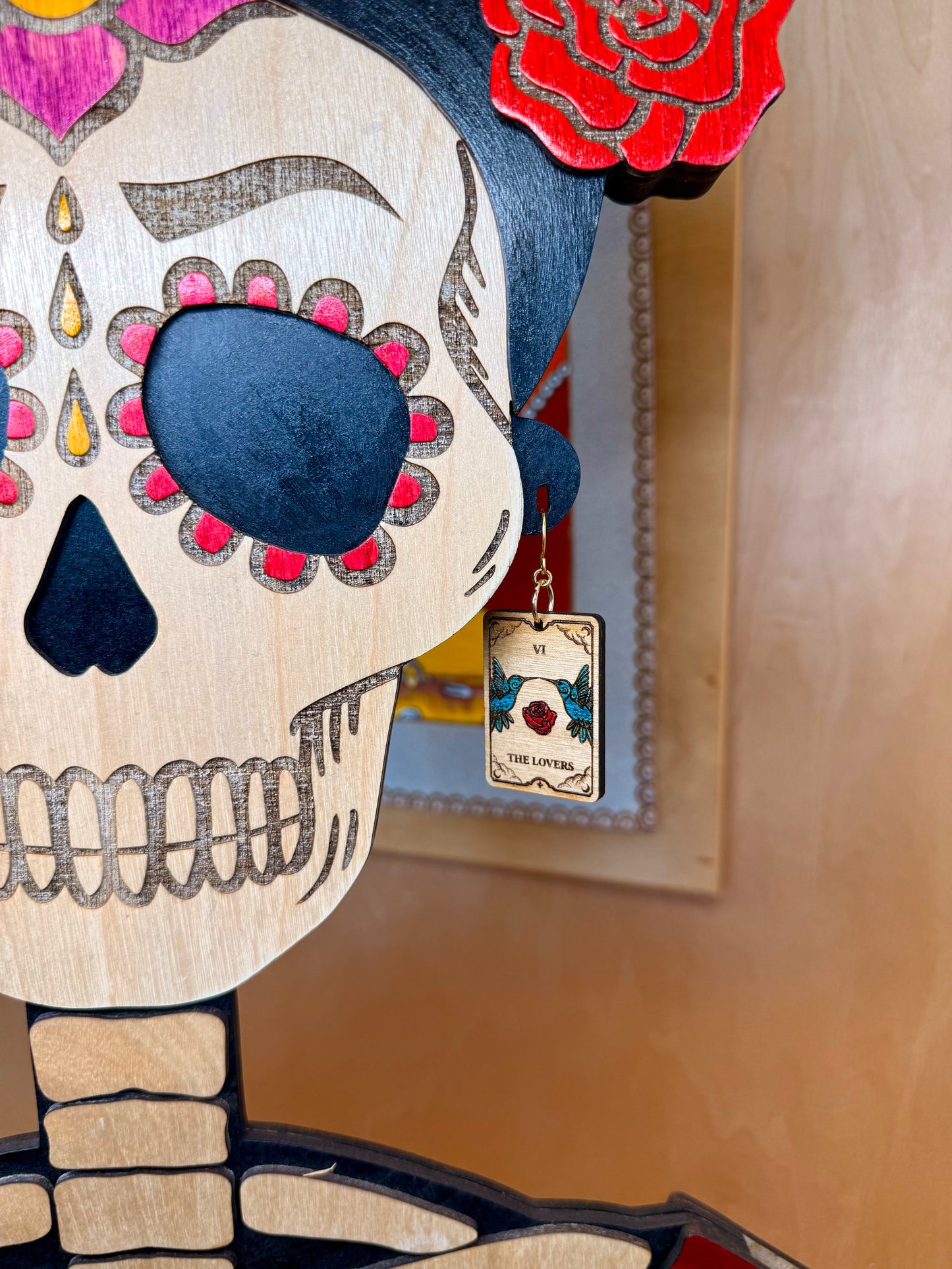 Decorative skull with Tarot the lovers card earrings with roses and hummingbirds on a blurred background.