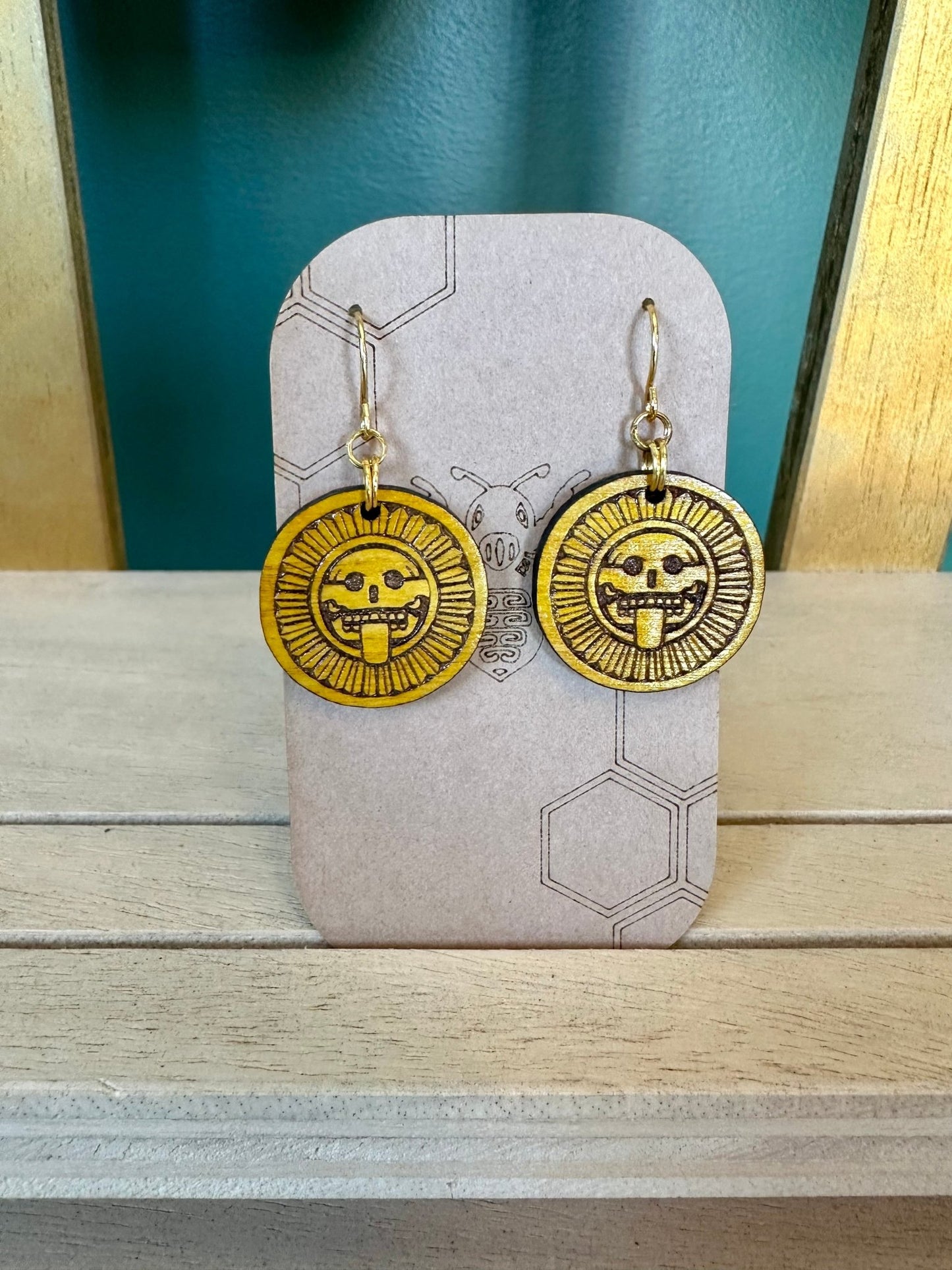 Mictlantecuhtli Stone Earrings wood engraved using gold colored hypoallergenic hooks. Earrings on a brown card stock earring holder.