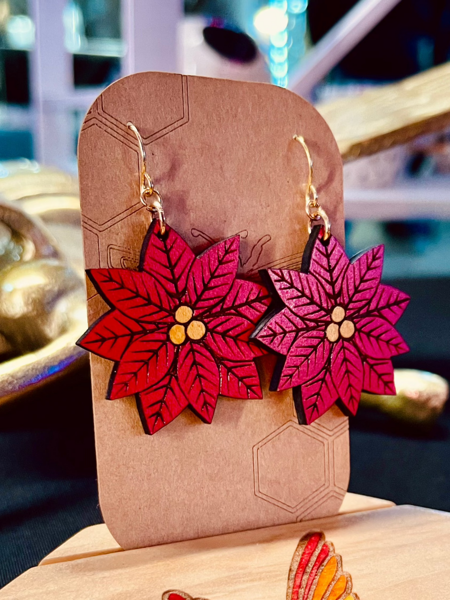 Wood engraved poinsetta noche buena red flower earrings on gold colored hypoallergenic nickel free hooks on a brown cardstock earring holder.