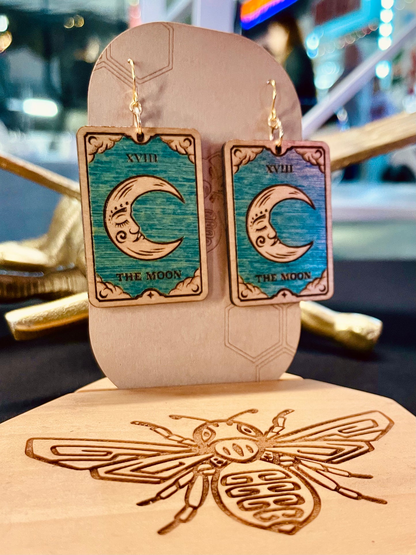 wood engraved tarot card depicting a crecent moon with blue sky background earrings on gold colored hypoallergenic nickel free hooks displayed on a brown cardstock earring holding.