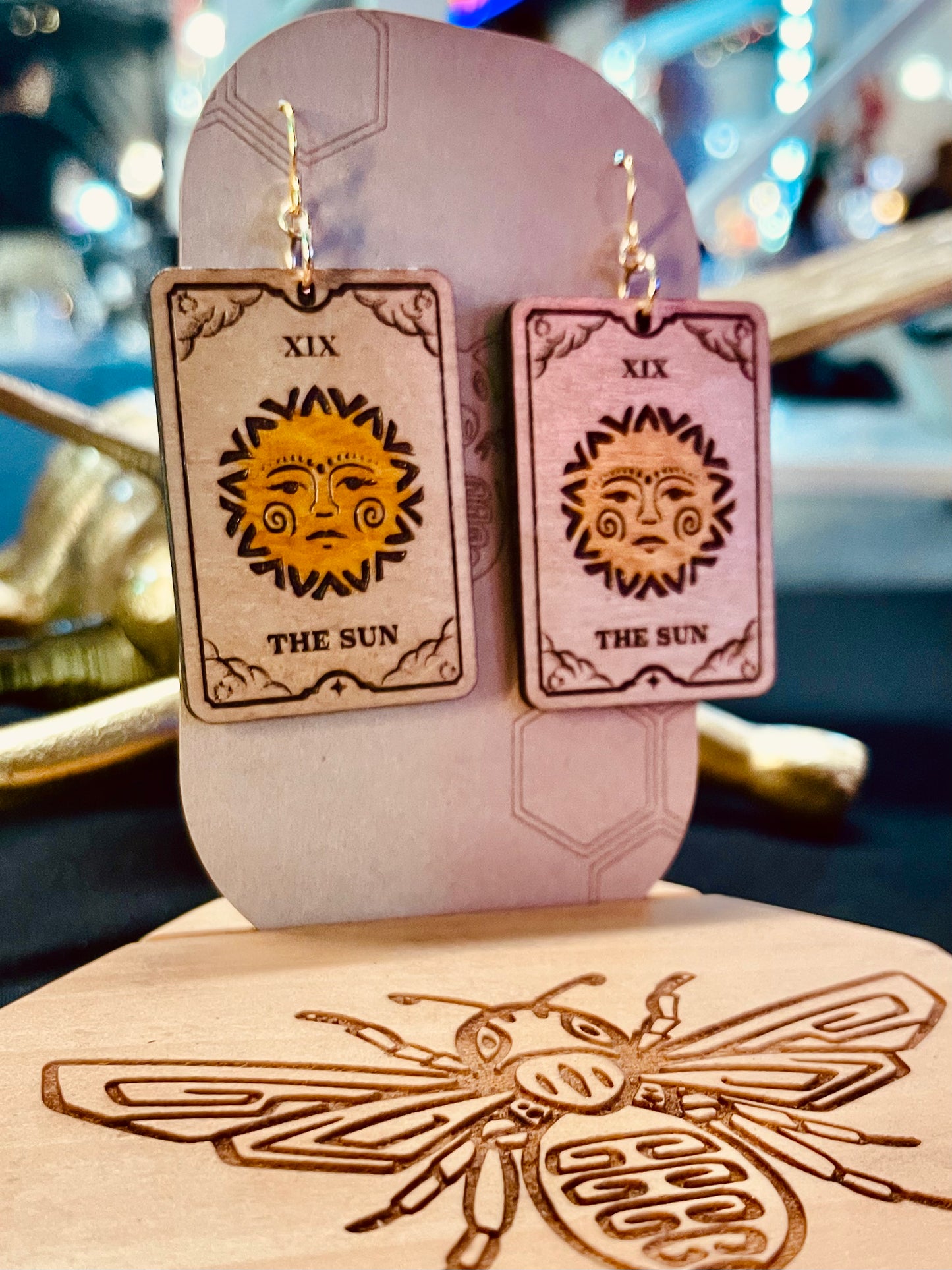 wood engraved the sun colored yellow tarot card earrings with gold colored hypoallergenic nickel free hooks on a brown cardstock earring holder.