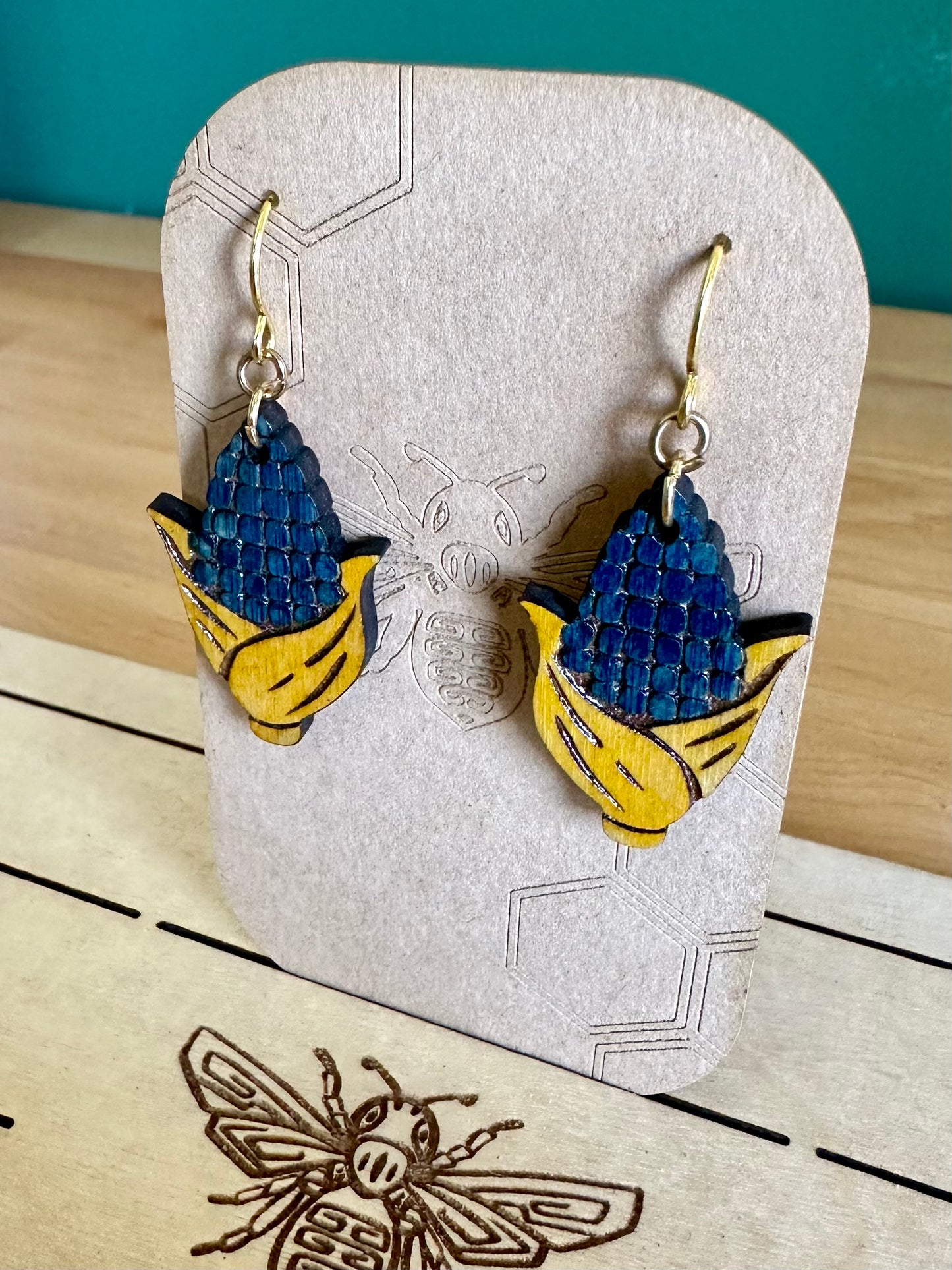 Blue and Yellow Wood Corn Earrings on gold colored hypoallergenic hooks on an earring card holder. 