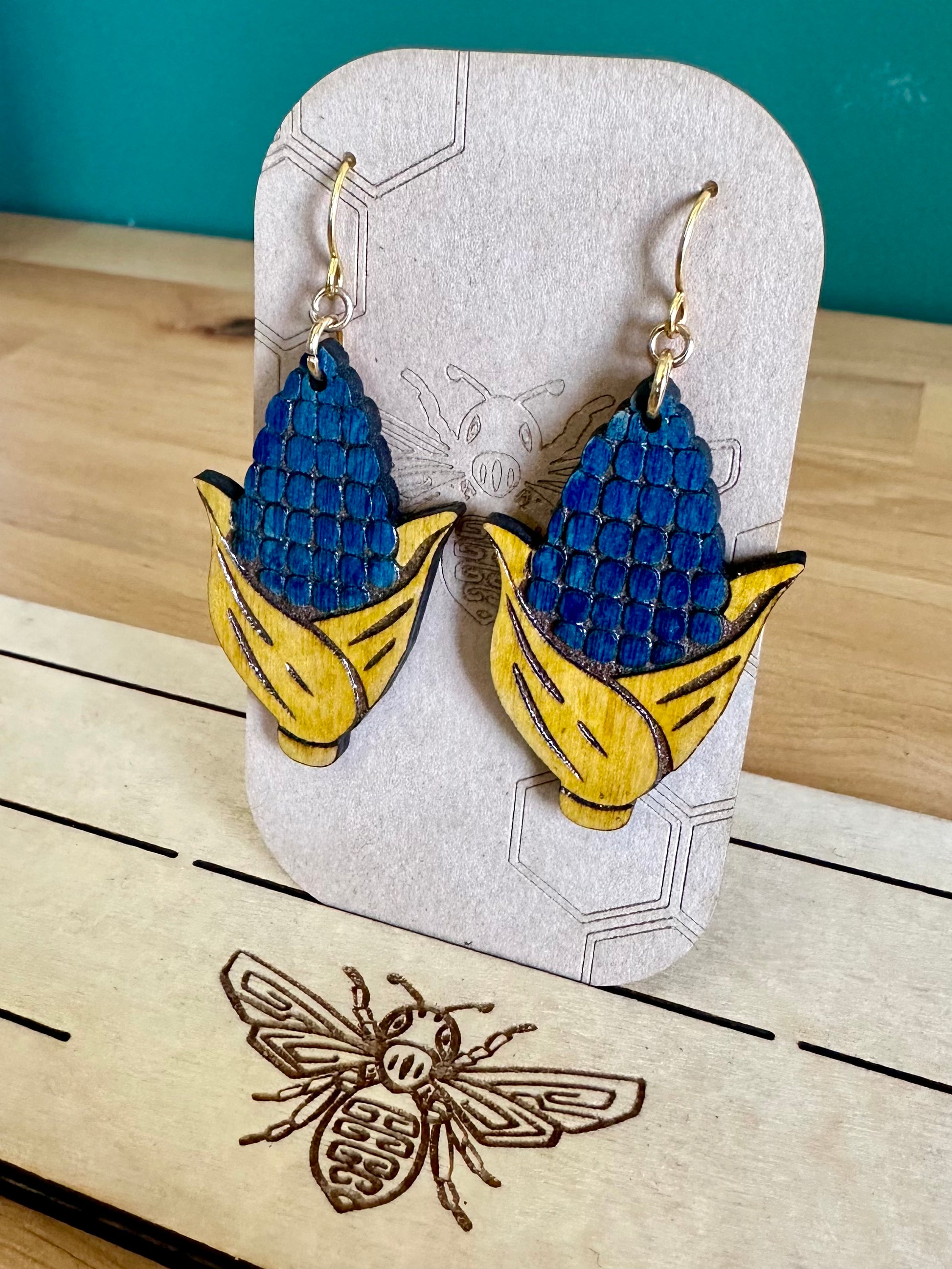 Blue and Yellow Wood Corn Earrings on gold colored hypoallergenic hooks on an earring card holder. 