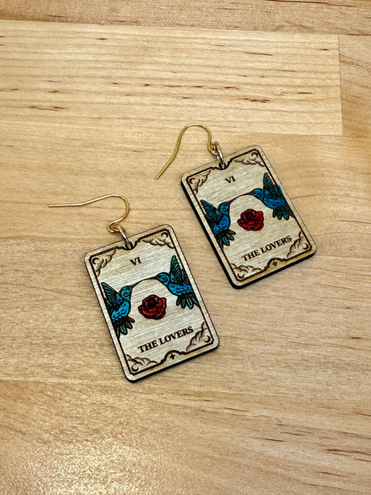 Tarot the lovers card earrings with roses and hummingbirds on a wooden surface.