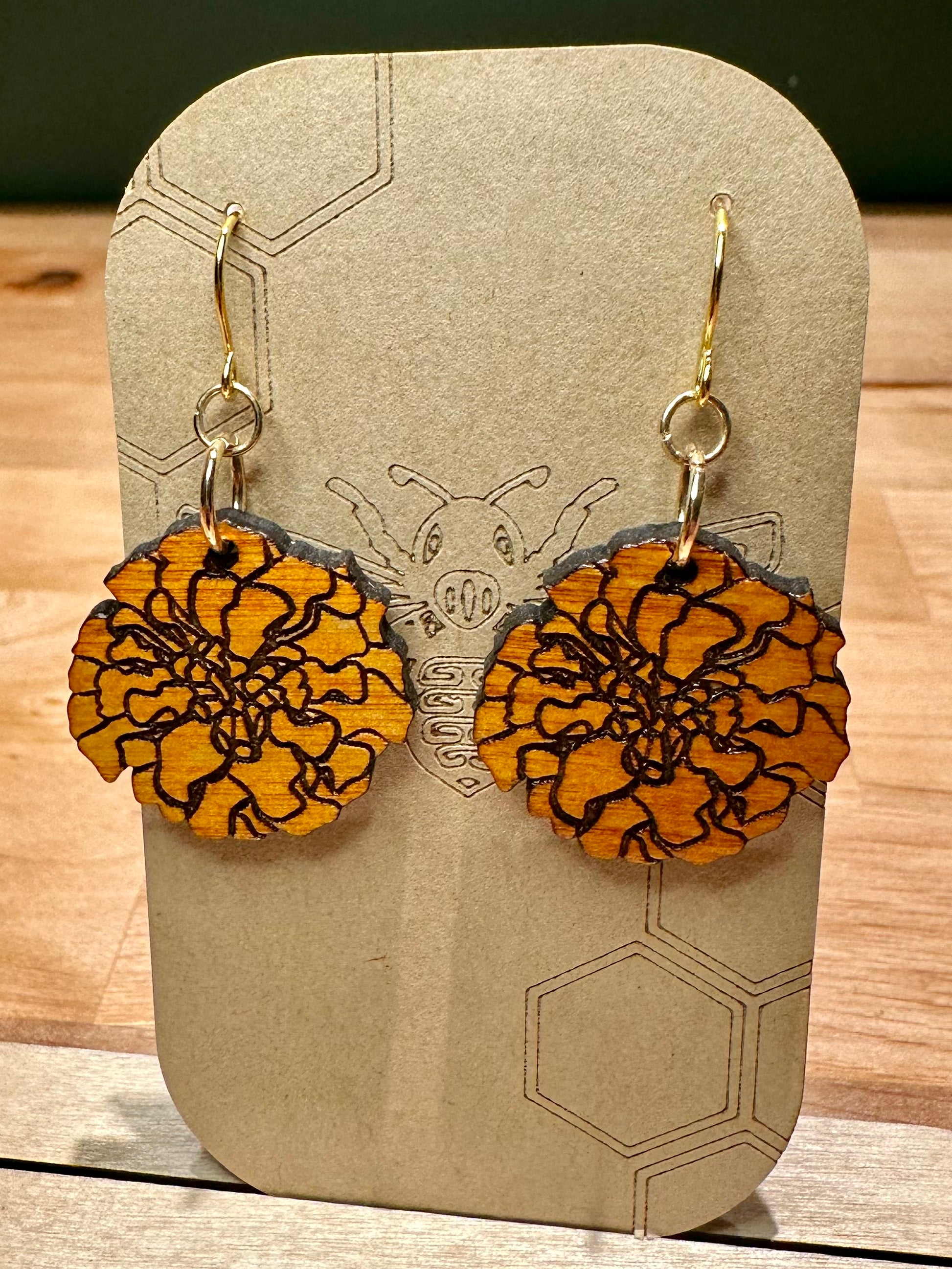 wood engraved orange marigold on gold colored hypoallergenic hooks on brown card stock earring holder. 