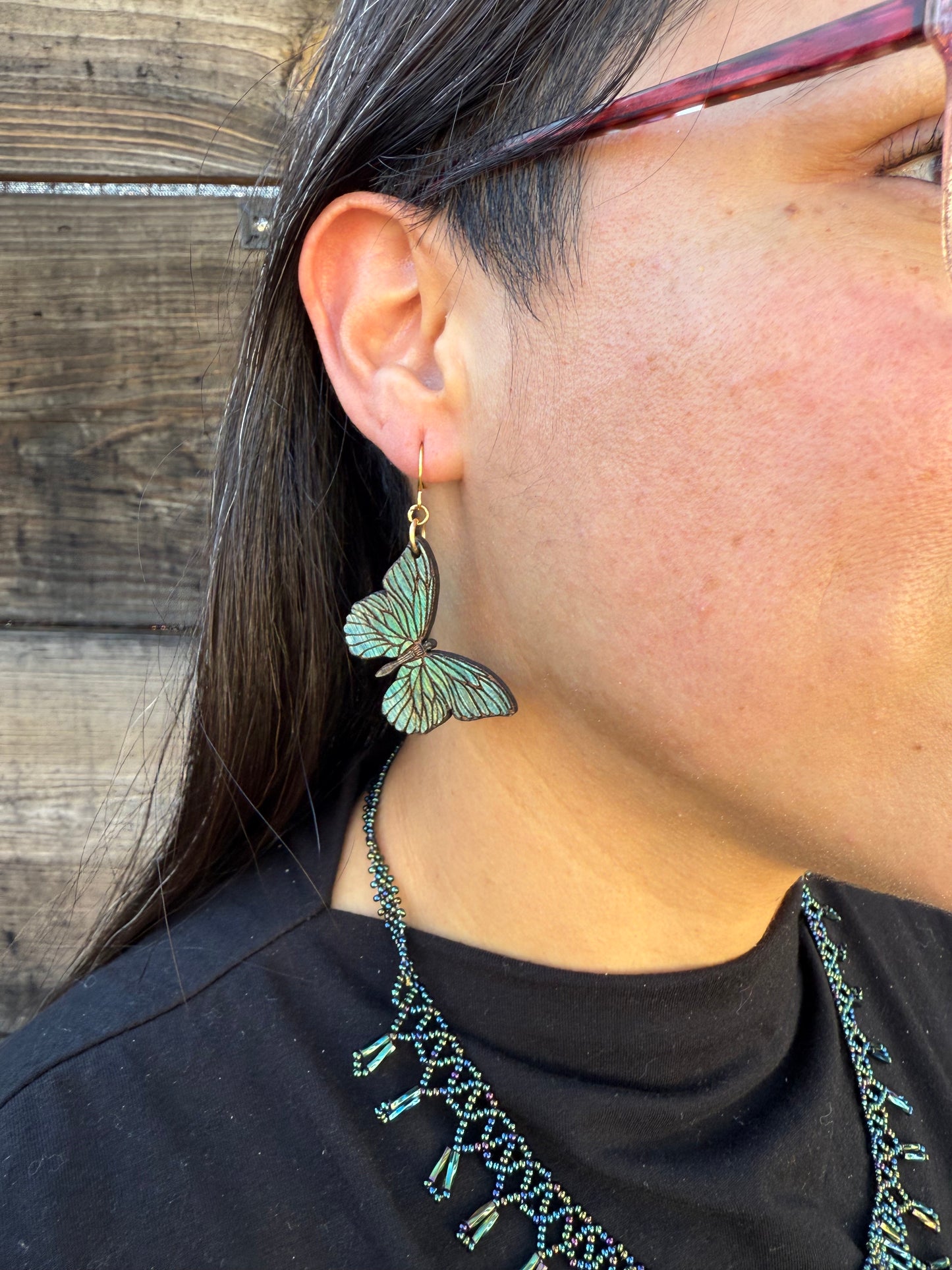 Butterfly earring worn by a person with a black top on a wooden surface.