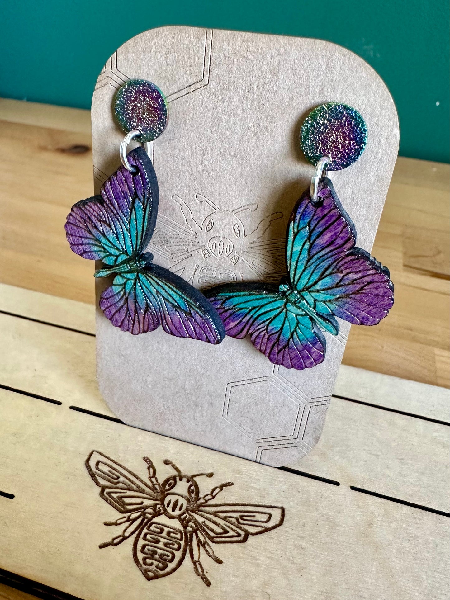 Dark to light shades of Blue and purple Wood Butterfly Earrings on silver colored hoops and purple and blue glittery stud earrings. 