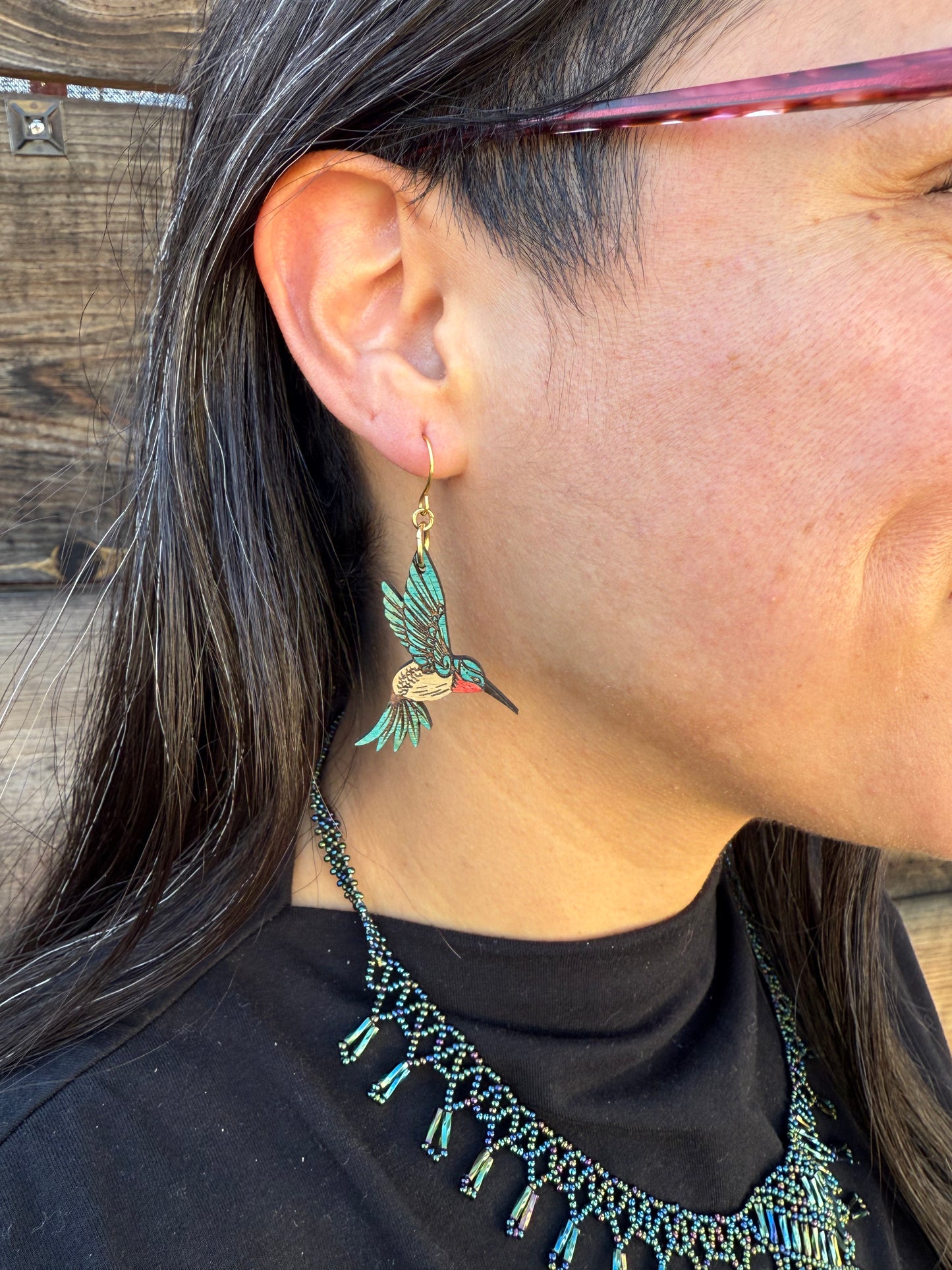 Person wearing a blue hummingbird earring and a black top with beaded details.