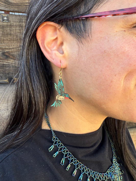 Person wearing a blue hummingbird earring and a black top with beaded details.