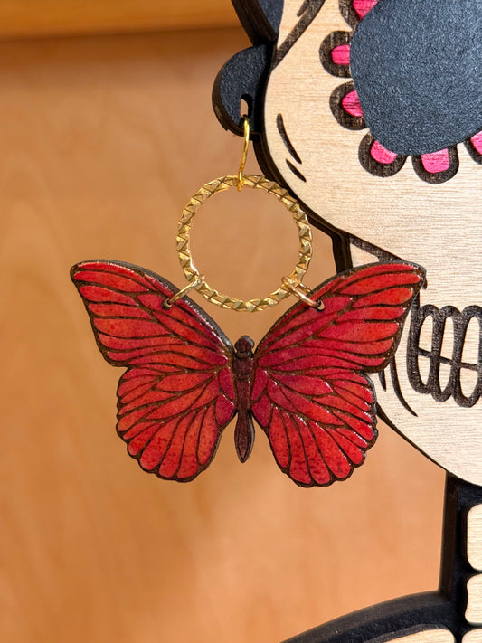 dark pink wood engraved butterfly earrings dangling on a gold textured circle. 