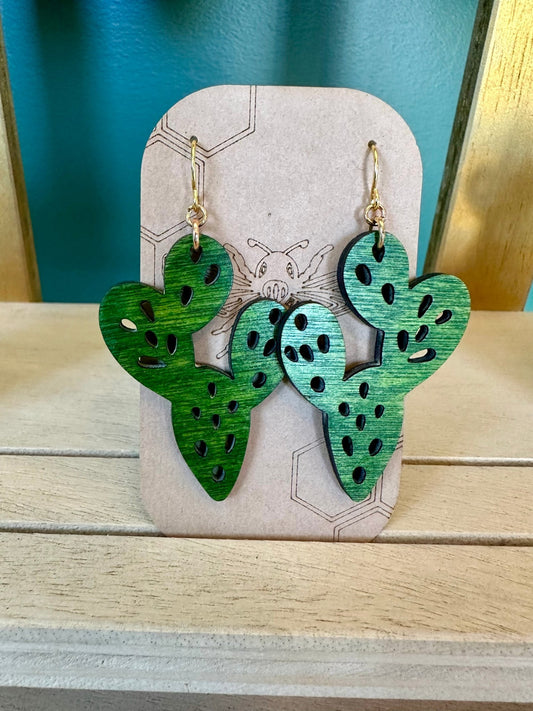 Green colored wood cactus earrings on a gold colored hypoallergenic earring hook. Earrings on a brown card stock earring holder. 