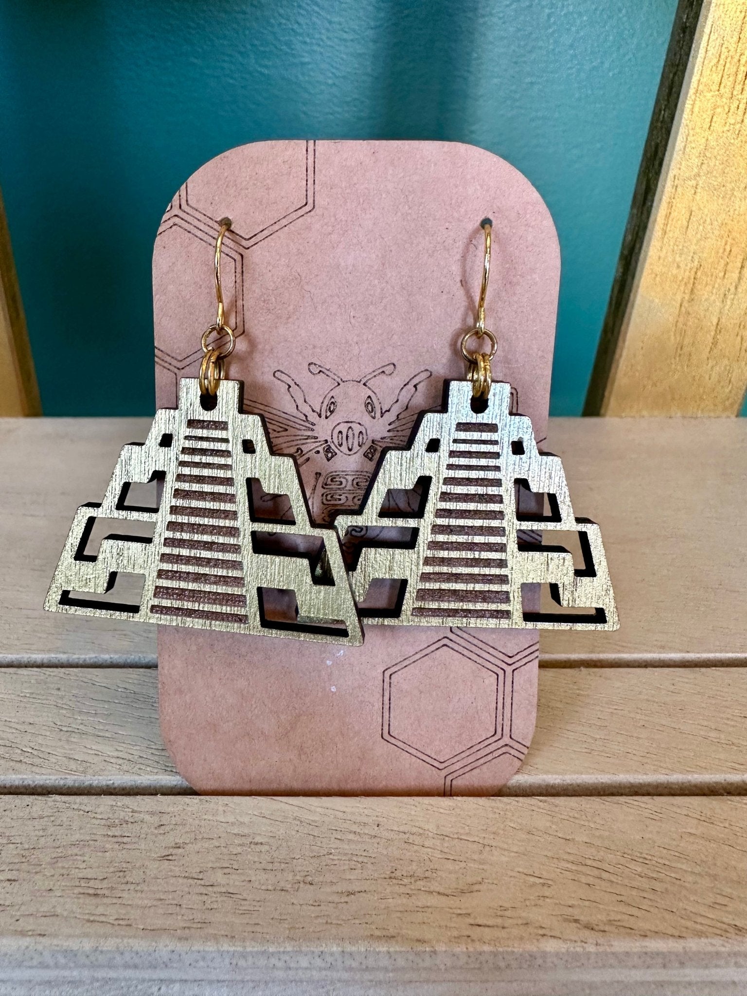 Gold colored wood chichen itza pyramid temple earrings on a gold colored hypoallergenic earring hook. Earrings on a brown card stock earring holder. 