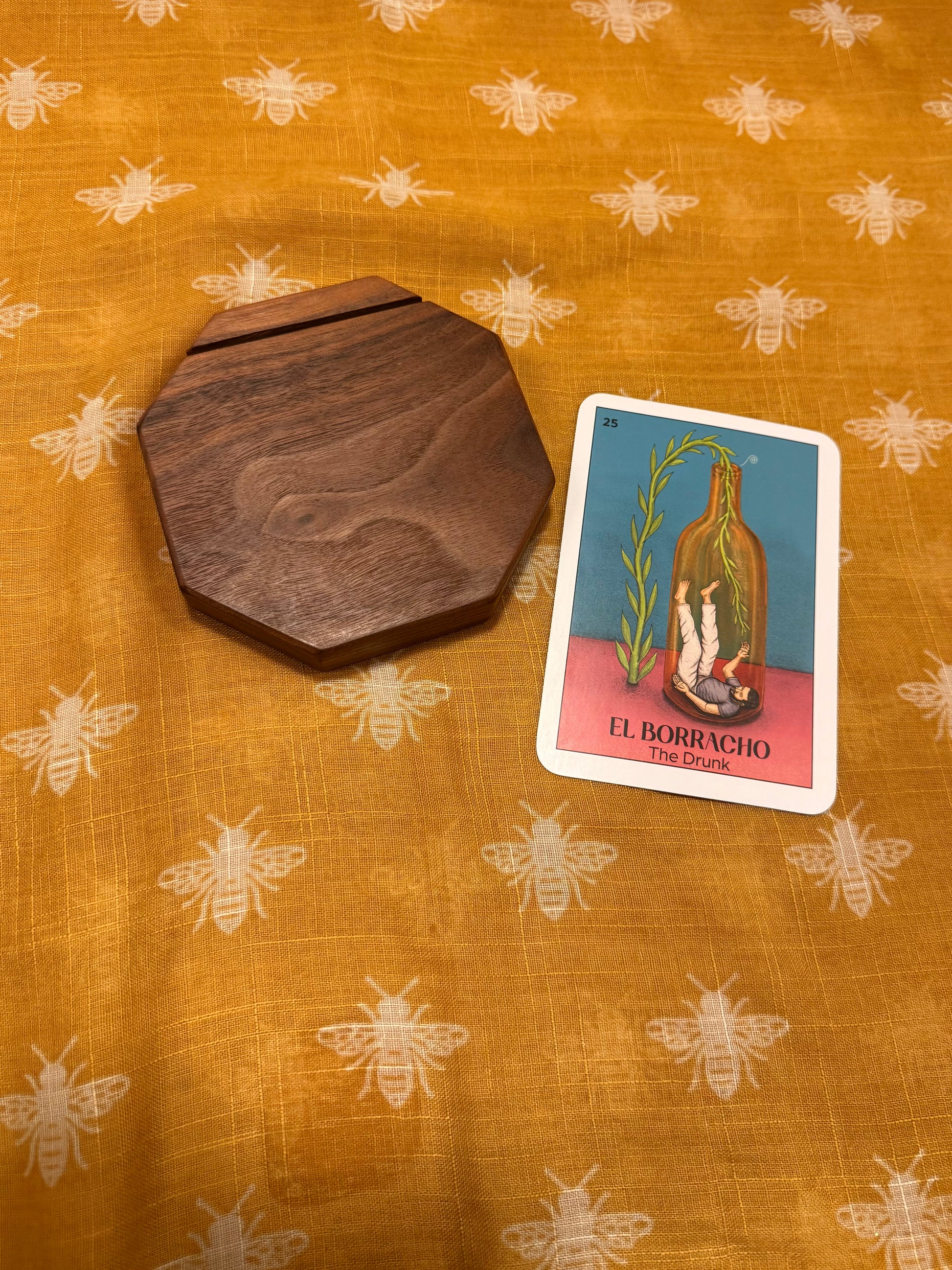 Dark walnut wooden tarot card holder and card on a patterned fabric background with bees.