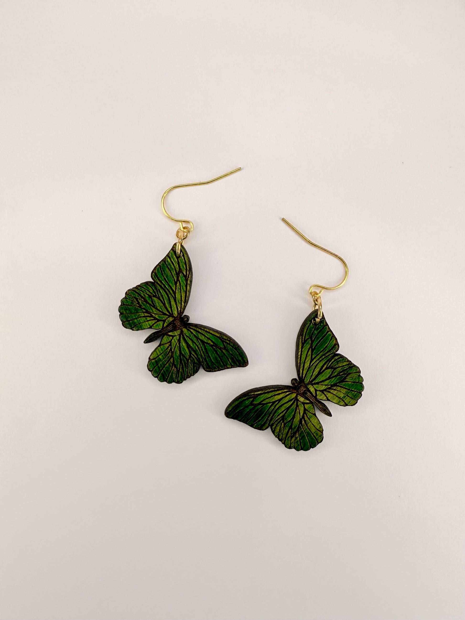 Green butterfly-shaped earrings on a white background.
