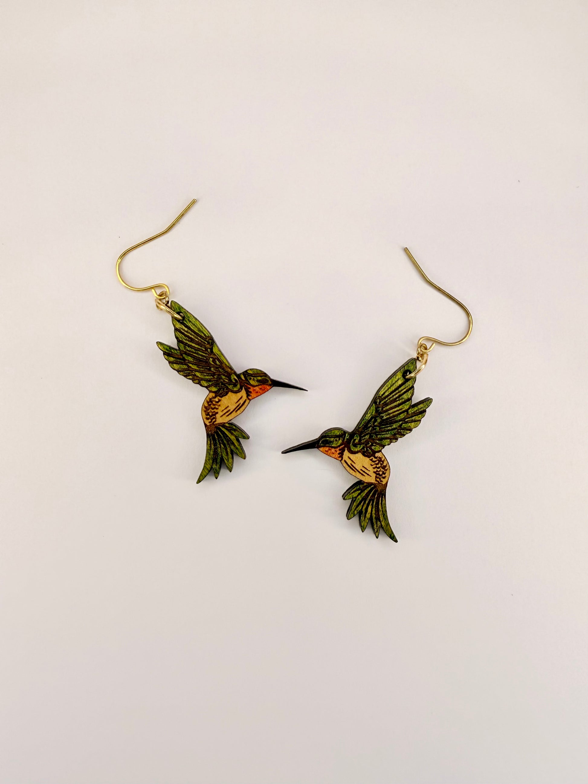 Green hummingbird earrings on a light beige background
