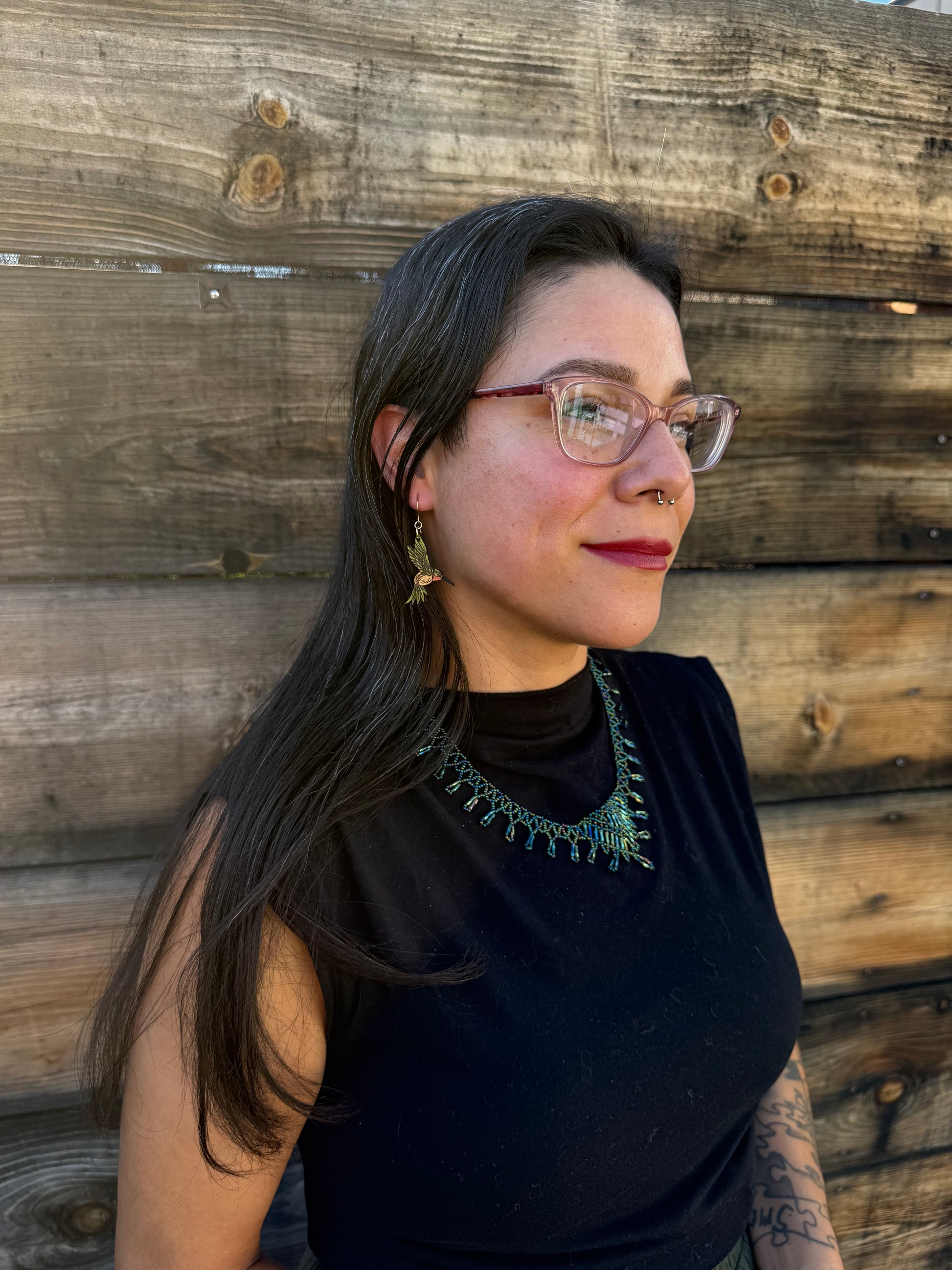 Person from a side angle wearing green hummingbird earrings.