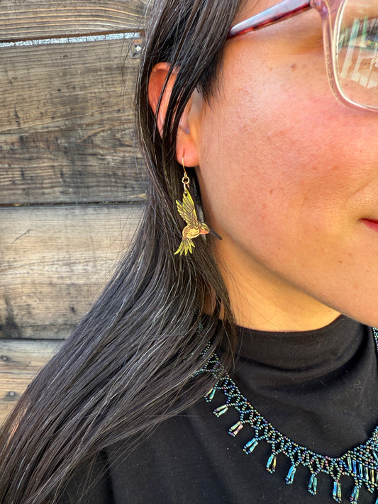 Up close of a person wearing green hummingbird earrings.