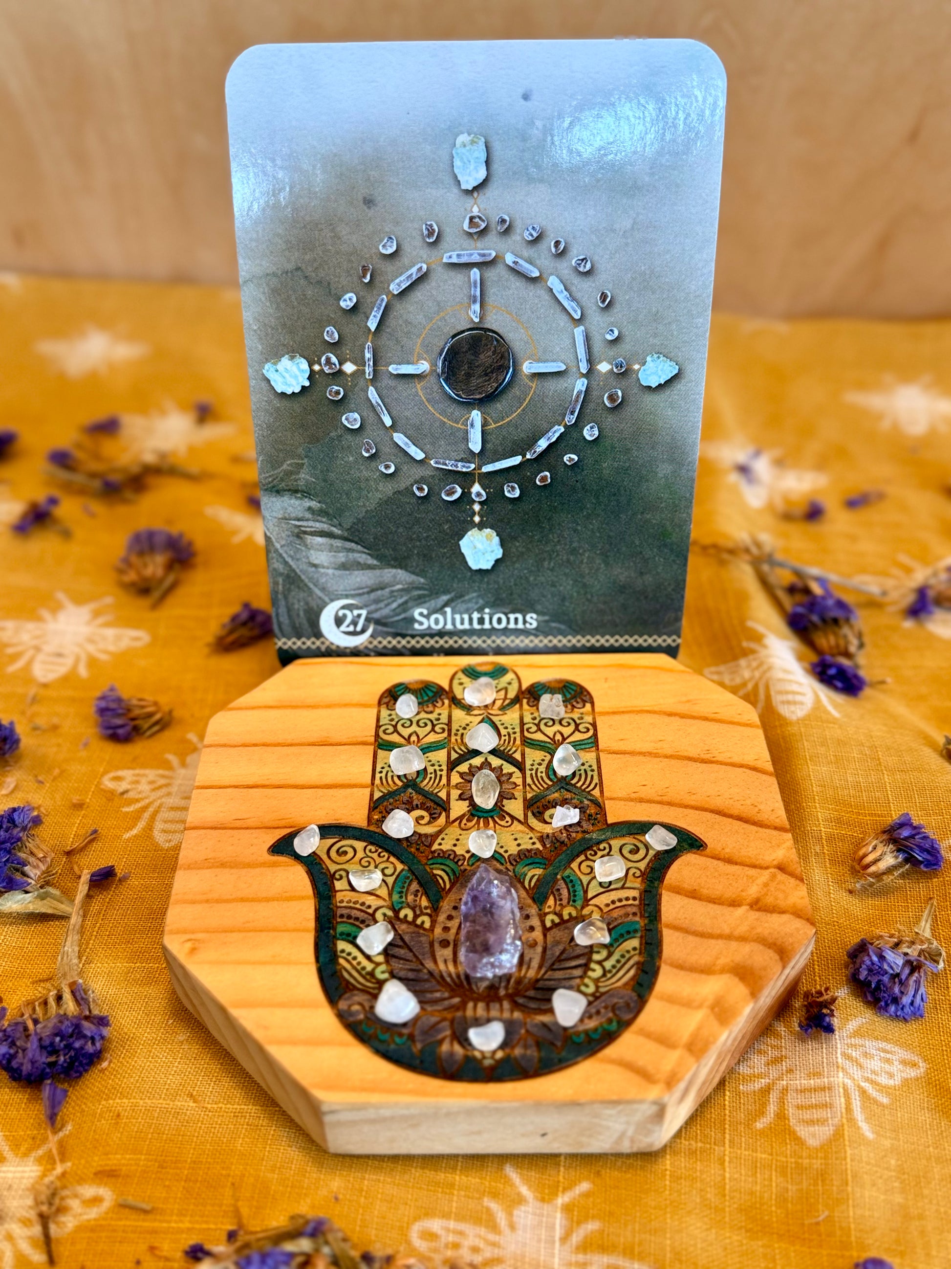 hamsa hand tarot card holder with crystals and flowers around it. 