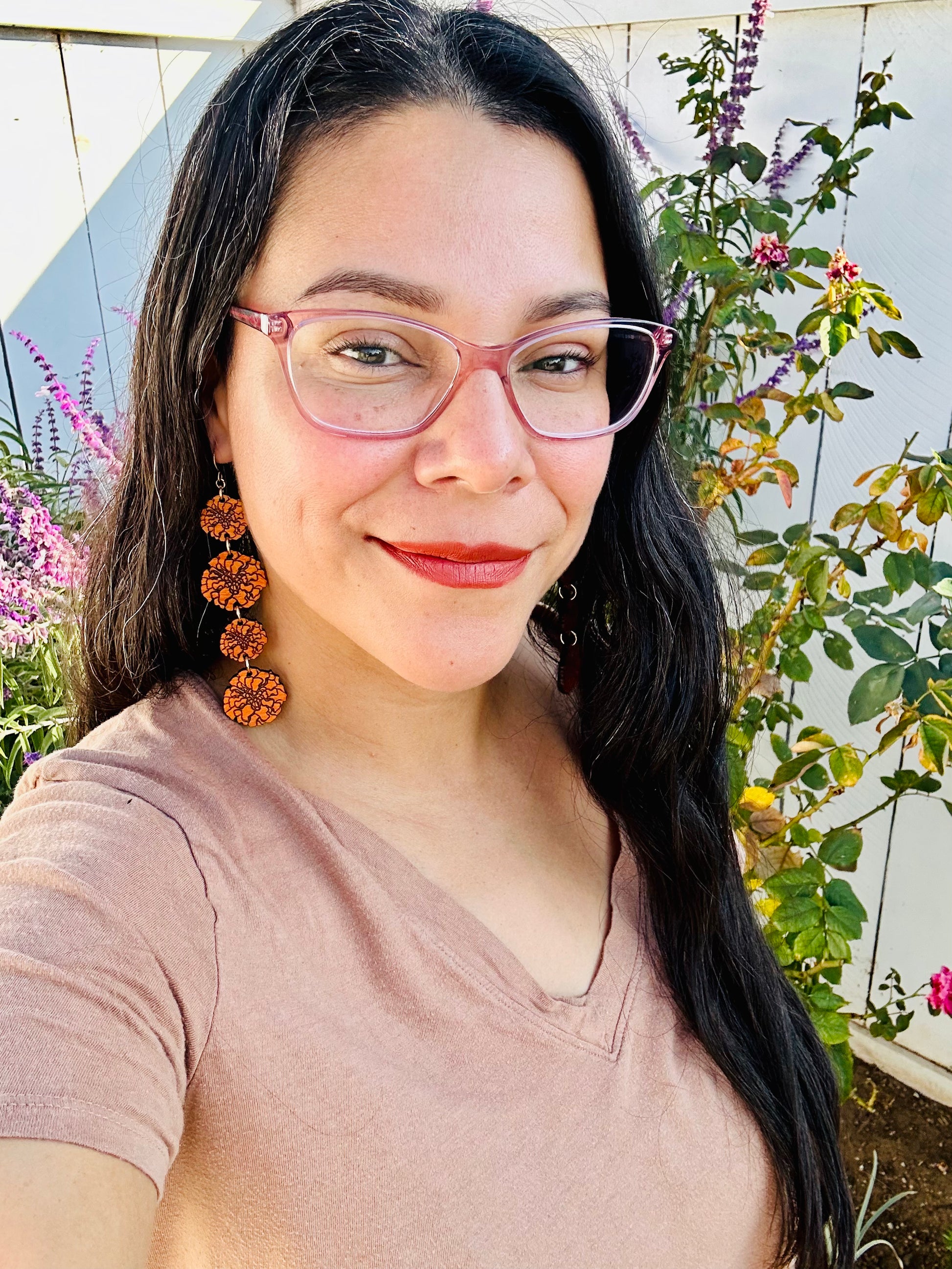 woman with long black and grey hair with glasses wearing wood engraved orange marigold 4 strand of different sizes earrings on gold colored hypoallergenic hooks. 