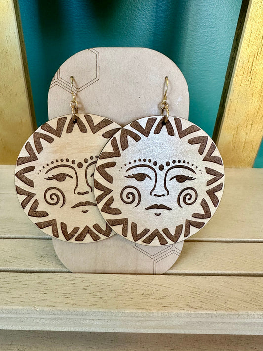 wood engraved natural wood toned sun with face earrings with gold colored hypoallergenic earring hooks. earrings on a brown card stock earring holder.