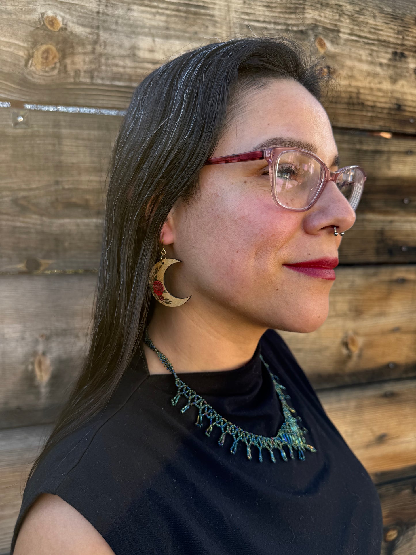 Woman wearing wooden crescent moon earrings with red rose engraving.