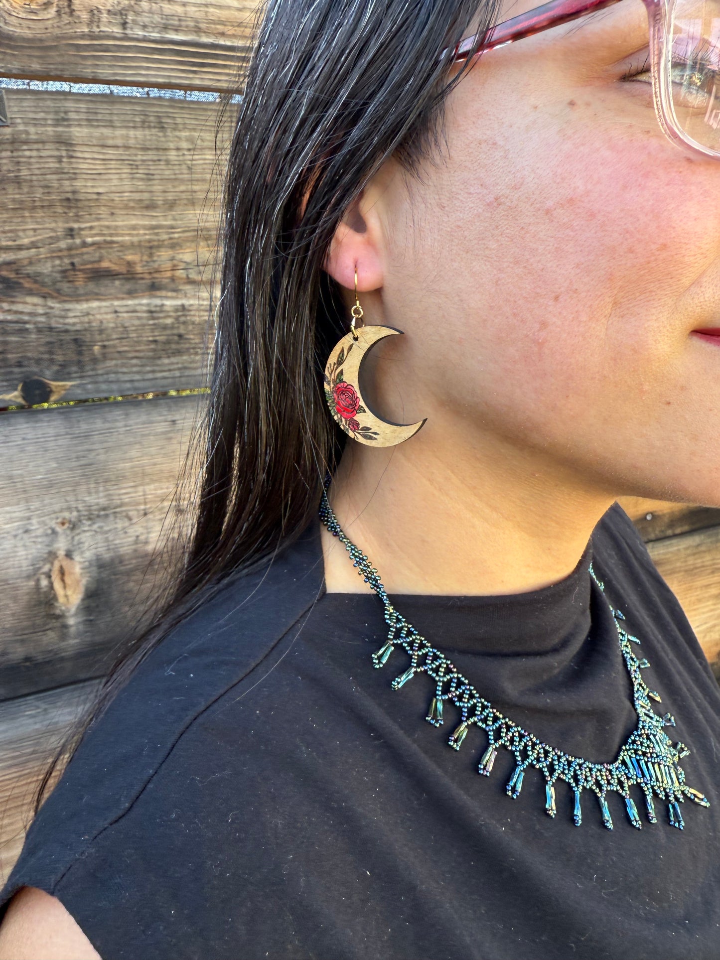 Up close of a person wearing wooden crescent moon earrings with red rose engraving.