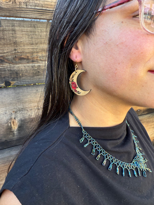 Up close of a person wearing wooden crescent moon earrings with red rose engraving.