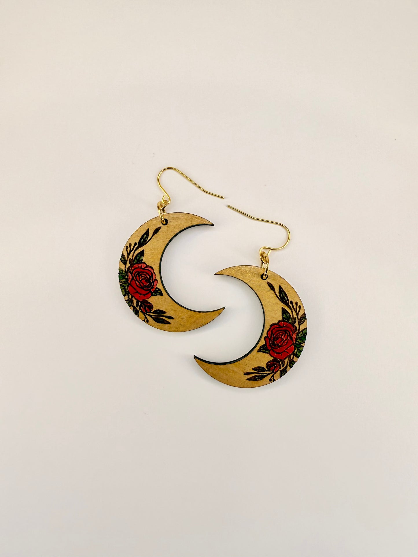 Crescent moon-shaped earrings with floral design on a beige background