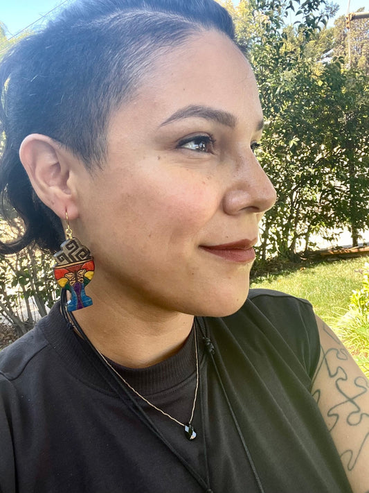 wood engraved rainbow colored Sahumerio Pride Earrings on a gold colored hypoallergenic earring hook being worn by a woman with hair in a ponytail looking to the side. 