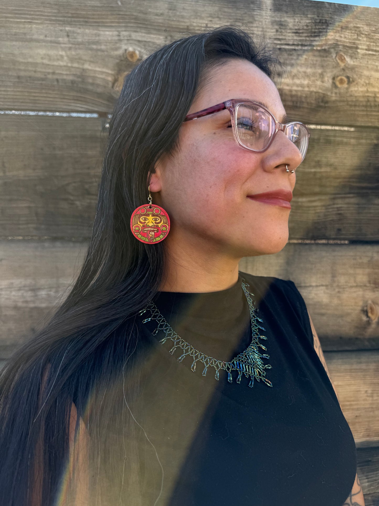 A side angle of a woman wearing red and yellow tonatiuh sun earrings.